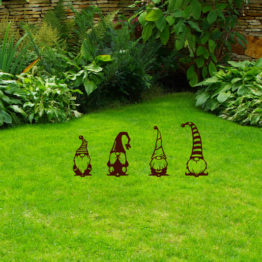 Four garden gnome decorations on a grassy lawn with a stone wall and plants in the background.