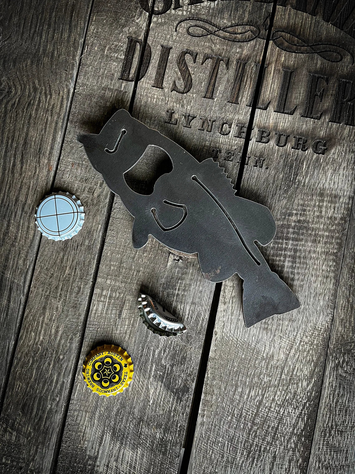 Metal fish-shaped bottle opener on a wooden surface with bottle caps.