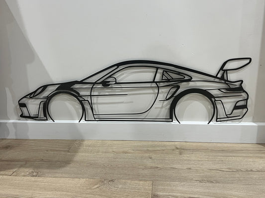 Car-shaped metal wall art on a white wall with wooden floor.